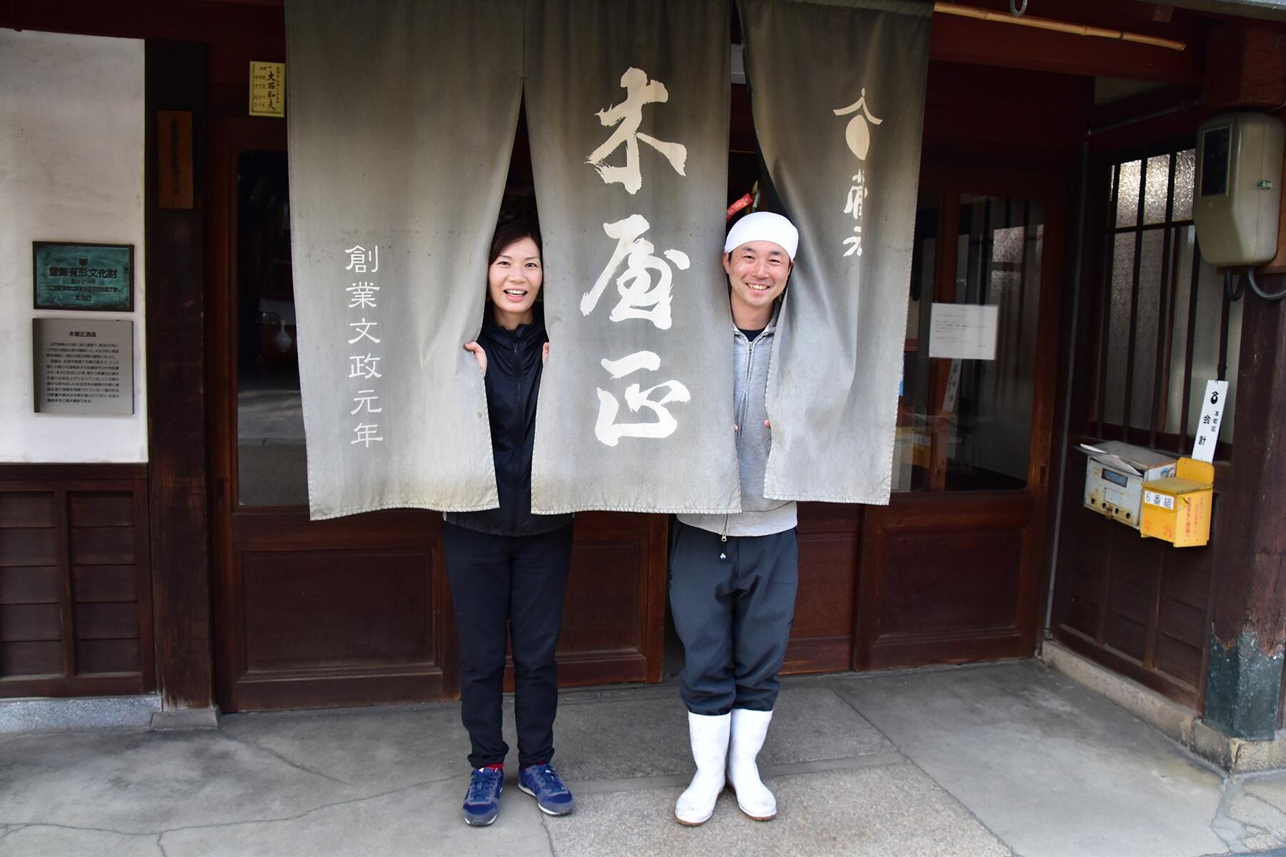 酒蔵の入口で、暖簾からひょっこり顔を出す大西さんと妻・香美さん