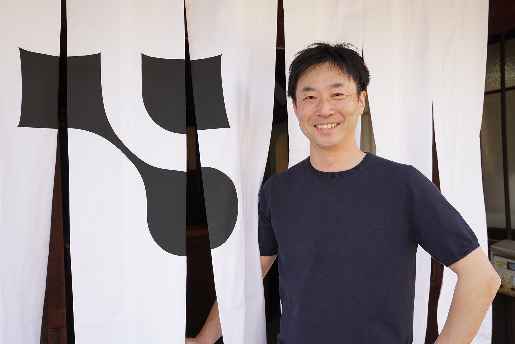 酒蔵入口の暖簾前に立つ大西さん