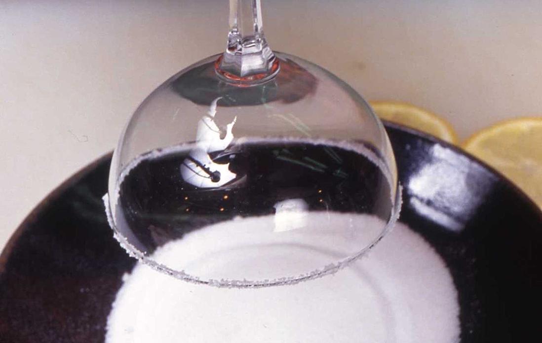 皿の上に塩をあけて、カクテルグラスの縁を回すように塩をつける。薄切りにしたレモンを1枚グラスの中に入れる。