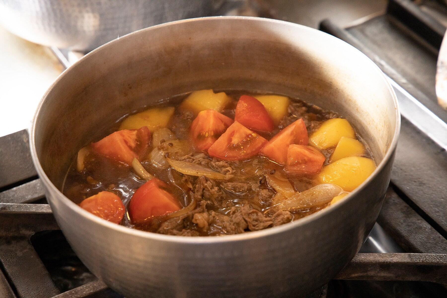 鍋にフライパンの玉ねぎと牛肉、乱切りにしたトマトを加えて7～8分煮る