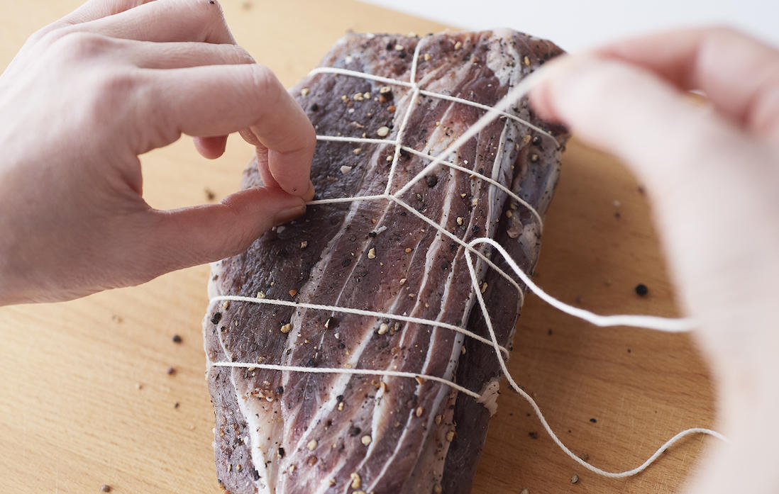 6、端まで縛ったら牛肉をひっくり返して、長く伸びている紐で牛肉に巻きついている紐を十文字になるように括っていく。